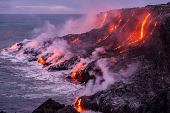 Lava Flows Entering the Ocean at Twilight Steam clouds rise from lava flowing into the ocean in Hawaii.