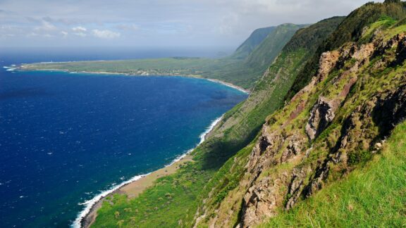 A view of steep sea-facing cliffs and the Kalaupapa Peninsula in the distance. 