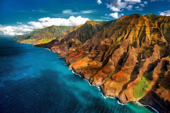 An aerial view of the Na Pali Coast in Hawaii with blue sky and clouds in the background.