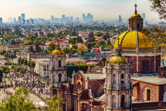 A view of Mexico City with the golden cupolas of a cathedral in the foreground. 