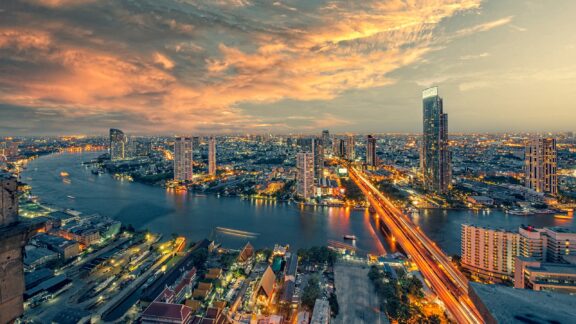 An aerial view of the Chao Phraya River and the surrounding urban landscape in Bangkok just before sunrise.