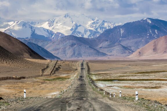 The Pamir Highway runs through a wide desert backed by snow-capped mountains.