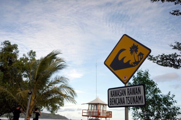 A yellow caution sign says “Tsunami prone area” in Indonesian.