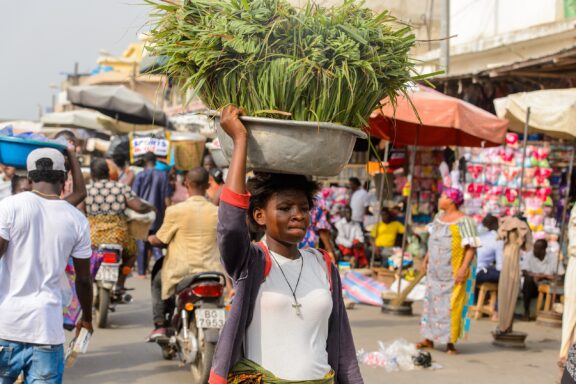 Market Vendor Carrying Produce on Head in Busy Street Market Woman balancing basin on her head, a common sight in Lomé