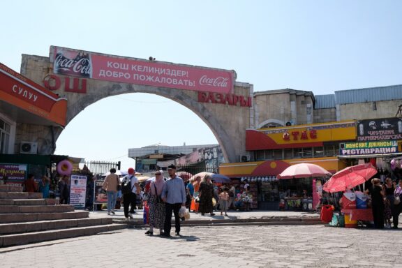Entrance of Osh Bazaar with People and Market Stalls Osh Bazaar, a cultural hub where traditions meet commerce