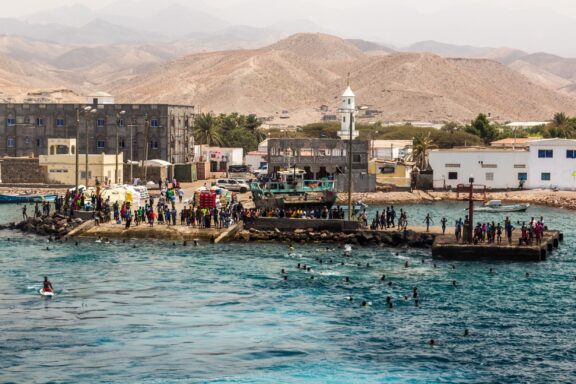 People stand on docks and swim in the water at the port of Tadjoura, Djibouti in the Red Sea.