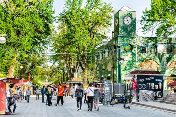 Pedestrians on a Tree-Lined Boulevard with Clock Tower Tashkent Broadway walking street, known for its artists, cafes, and vendors