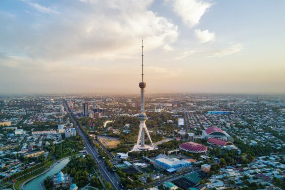 An aerial view of the Tashkent Television Tower standing tall over the capital of Uzbekistan at sunset.