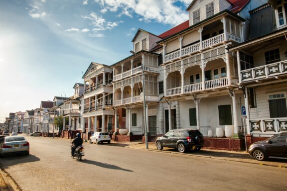 Colonial Architecture on a Sunny Street with Motorcyclist Waterkant Street, lined with colonial-era buildings