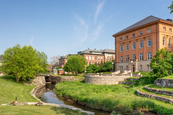 A creek flows between university buildings and grass.