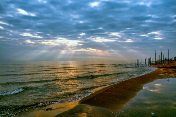 The sun shines through the clouds over the water at Bandar-e Anzali Port in the morning.