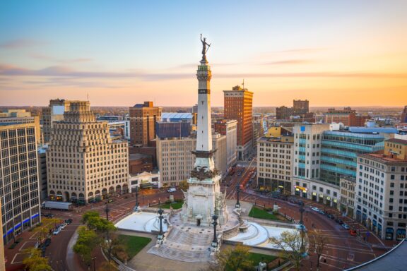 A monument stands in the middle of a roundabout in the middle of Indianapolis near sunset. 