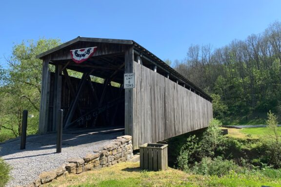 A view of the wooden Johnson Creek Covered Bridge with surrounding trees on a sunny, clear day.