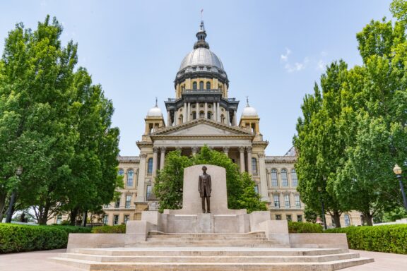 A statue of Abraham Lincoln stands in front of the Illinois State Capitol.