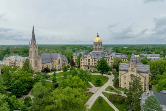 An aerial view of buildings in the Notre Dame University campus surrounded by trees.