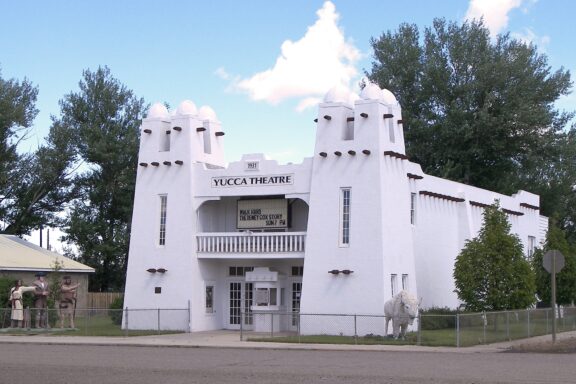 A view of the Yucca Theater standing near a road in Hysham, Montana under a partly cloudy sky.