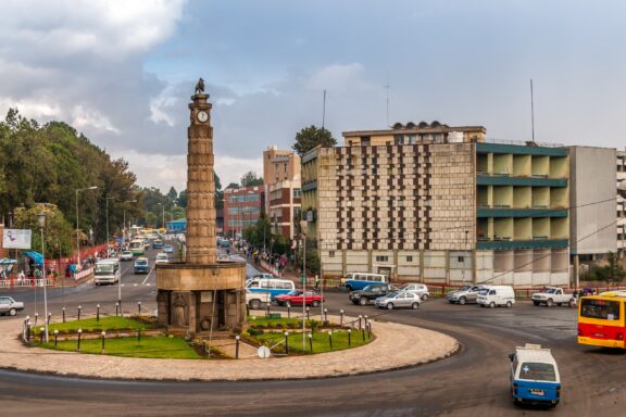 Cars and buses travel around the clock tower in the center of an Addis Ababa roundabout.