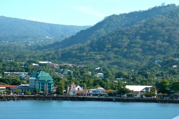 Coastal Town with Mountainous Backdrop The cityscape of Apia, a bustling urban center set against verdant hills and the Pacific Ocean