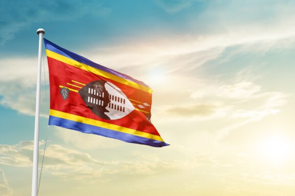 Eswatini Flag Against Sky Flag of Eswatini waving against a blue sky with clouds.