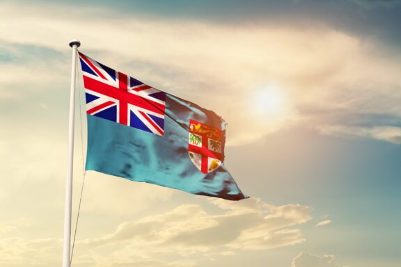 Flag of Fiji waving against a cloudy sky backdrop.