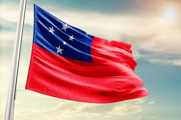 Flag of Samoa waving in the breeze against a cloudy sky.