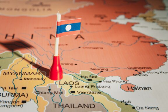 A small flag pin marking Laos on a colorful map, with neighboring countries China, Myanmar, and Thailand visible.