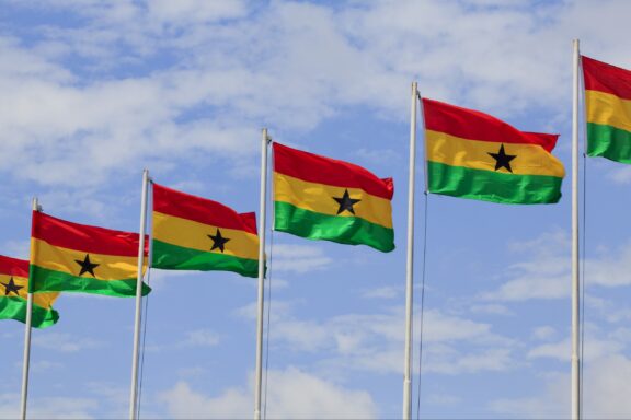 Multiple Ghanaian flags fluttering against a blue sky with clouds.