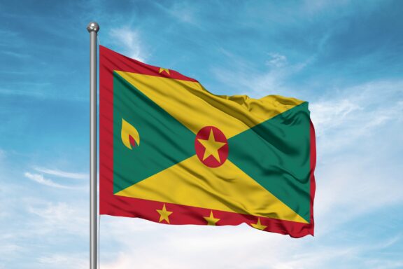 The national flag of Grenada waving against a blue sky with clouds.