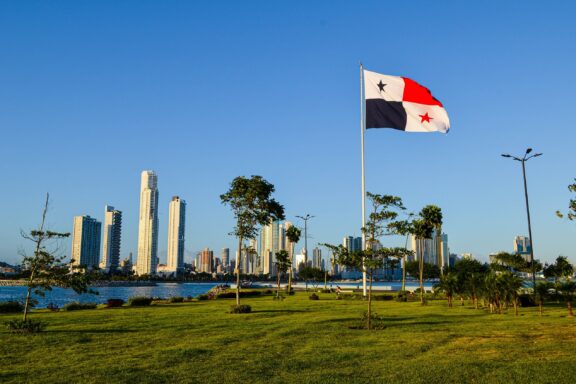 Panama flag waving in front of the Panama City skyline on a clear day.