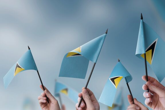 Multiple hands waving the flag of Saint Lucia against a cloudy sky.