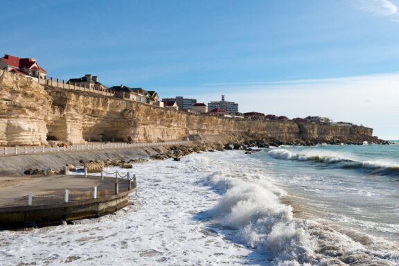 Waves crash against the shore below houses sitting on a cliff in Aktau, Kazakhstan.