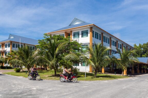 Government Building in Tuvalu with People on Motorbikes The Government House in Funafuti, a symbol of Tuvalu's journey toward self-governance