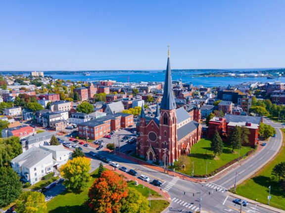 An aerial view of a cathedral in Portland, Maine backed by blue water.