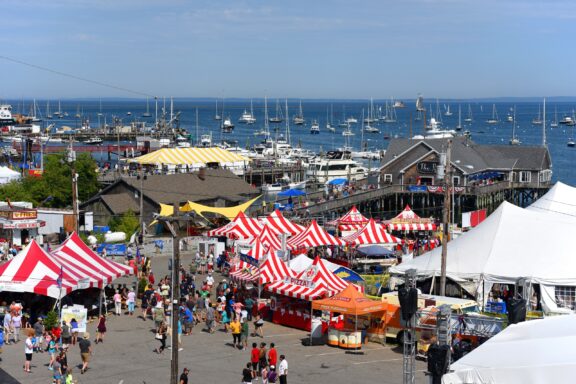 A view of people, vendors, and boats in Rockland, Maine on a sunny day during the Maine Lobster Festival.