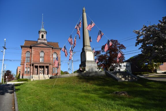 A low-angle view of the courthouse and a monument with American flags in Bath, Maine.