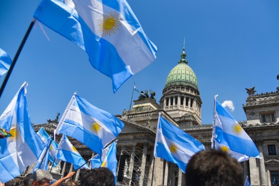 Argentinian flags waving in front of the Congress building in Buenos Aires under a clear blue sky.