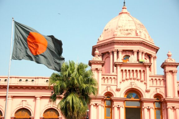 Bangladesh flag waving in front of a historic building with a dome in Dhaka.