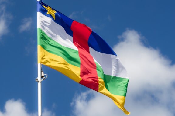 Flag of the Central African Republic waving against a blue sky with clouds.