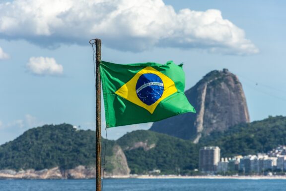 Brazilian flag waving with Copacabana beach and Sugarloaf Mountain in the background.