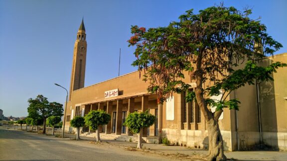 A street-level view of a clock tower standing next to a building in El Mahalla, Egypt.