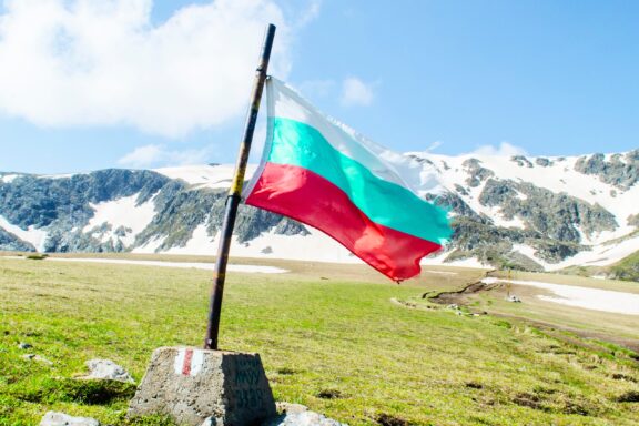 Bulgarian flag waving with Rila National Park's snowy mountains in the background.