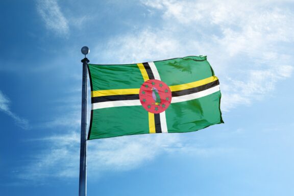 Flag of Dominica waving against a clear blue sky.