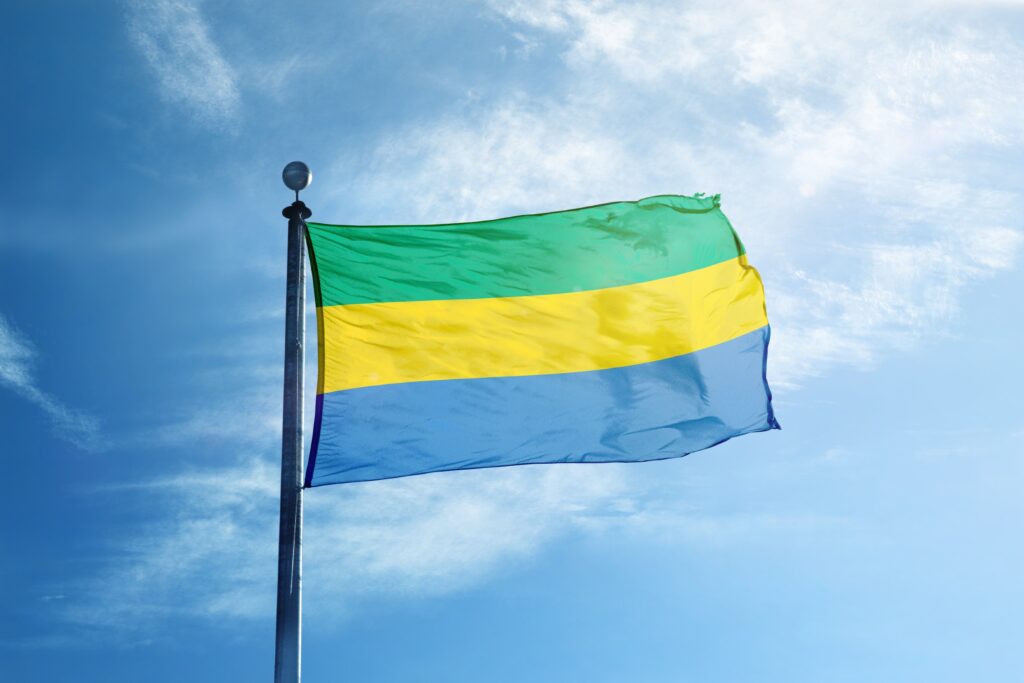 Flag of Gabon waving against a blue sky with light clouds.