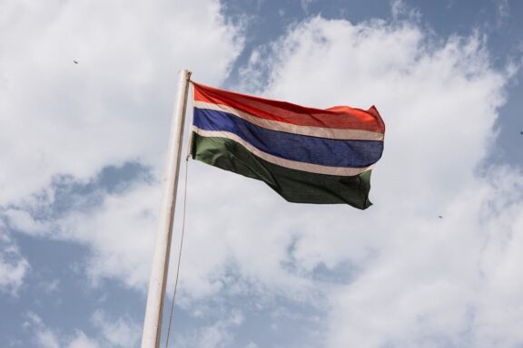 The flag of The Gambia waving against a cloudy sky.