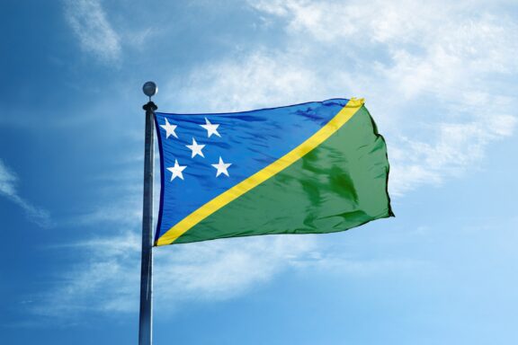 Flag of the Solomon Islands Against Blue Sky Flag of the Solomon Islands waving against a blue sky with light clouds.