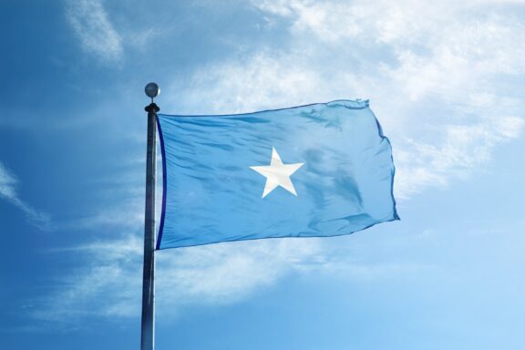 The flag of Somalia waving against a blue sky with light clouds.