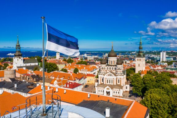 Estonian flag waving above the scenic old town of Tallinn under a clear blue sky.