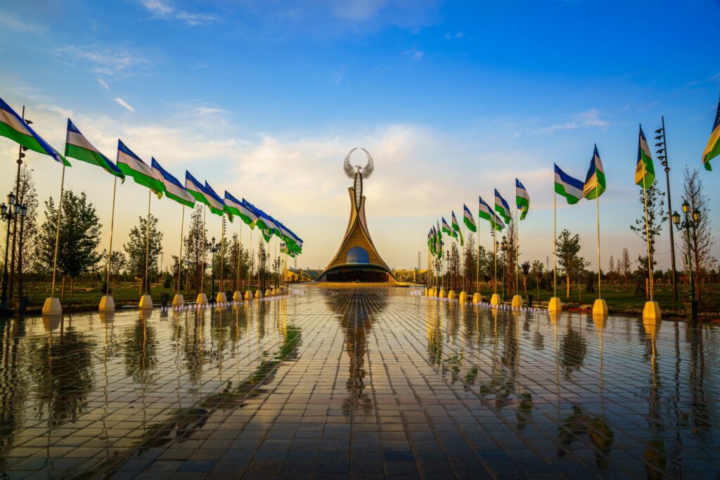 Independence Monument in Tashkent with Uzbek flags and reflecting pool at dusk.