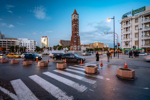 Cars and people pass each other in the city of Tunis during twilight.