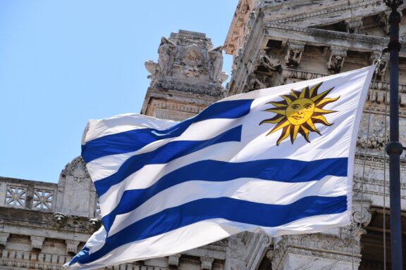 Uruguayan flag waving in front of a building with classical architecture.